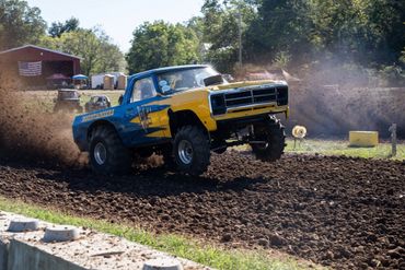 A lifted truck with 'Mountaineers' logo kicking up dirt on a muddy track.