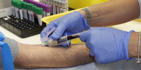 IHealthcare worker drawing blood from a patient's arm using a syringe.