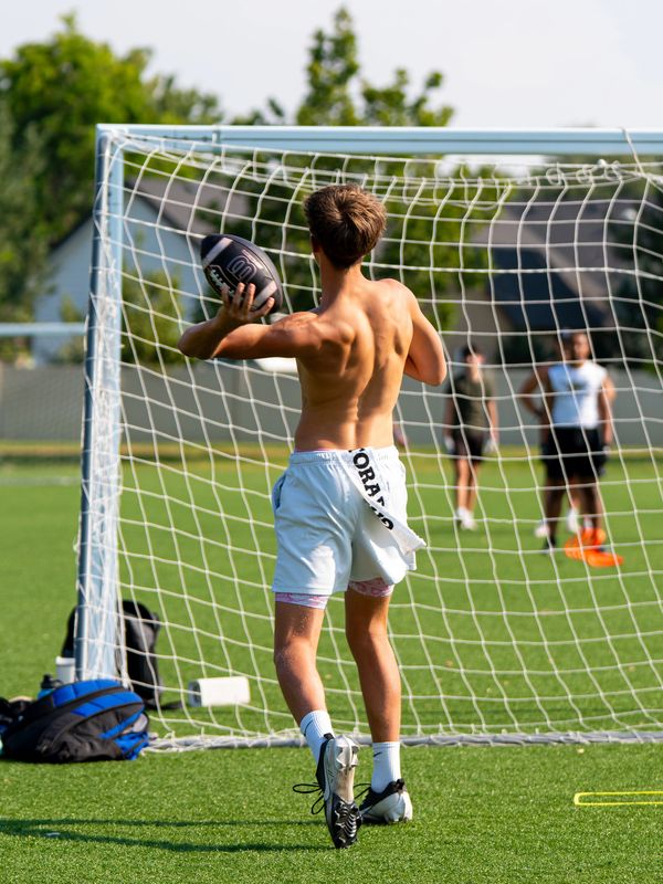 Shirtless young athlete prepares to throw a football on a sunny field.