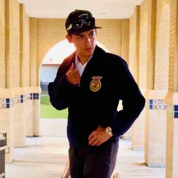 Young man in FFA jacket and cap posing indoors.