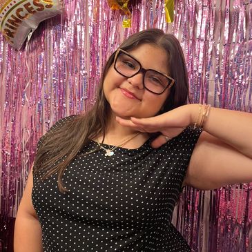 Smiling woman posing in front of pink shiny backdrop.