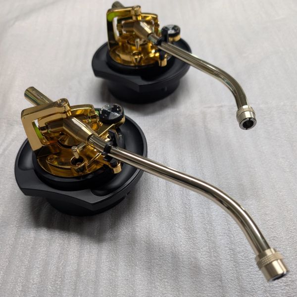 Two gold and black tonearm assemblies for turntables on a white surface.
