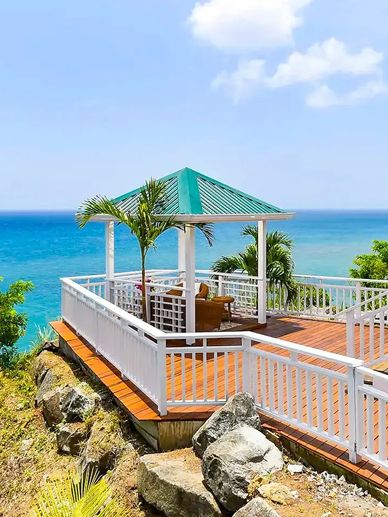 Oceanfront gazebo deck with seating and tropical plants overlooking the sea.