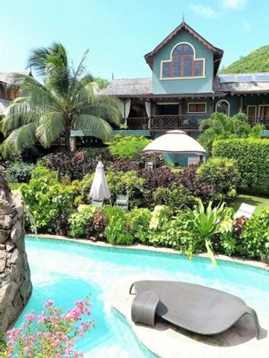 Tropical house with lush garden and a curved pool featuring a stone arch.