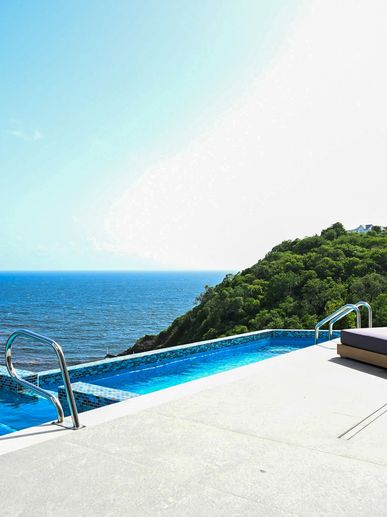 Infinity pool overlooking the ocean with lounge chairs on a sunny day.