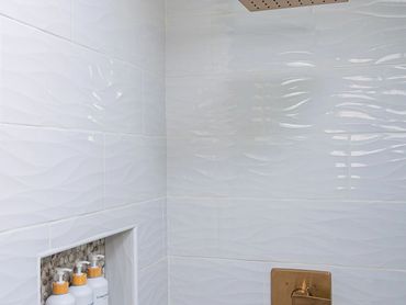 Modern shower with gold fixtures and white textured tiles.