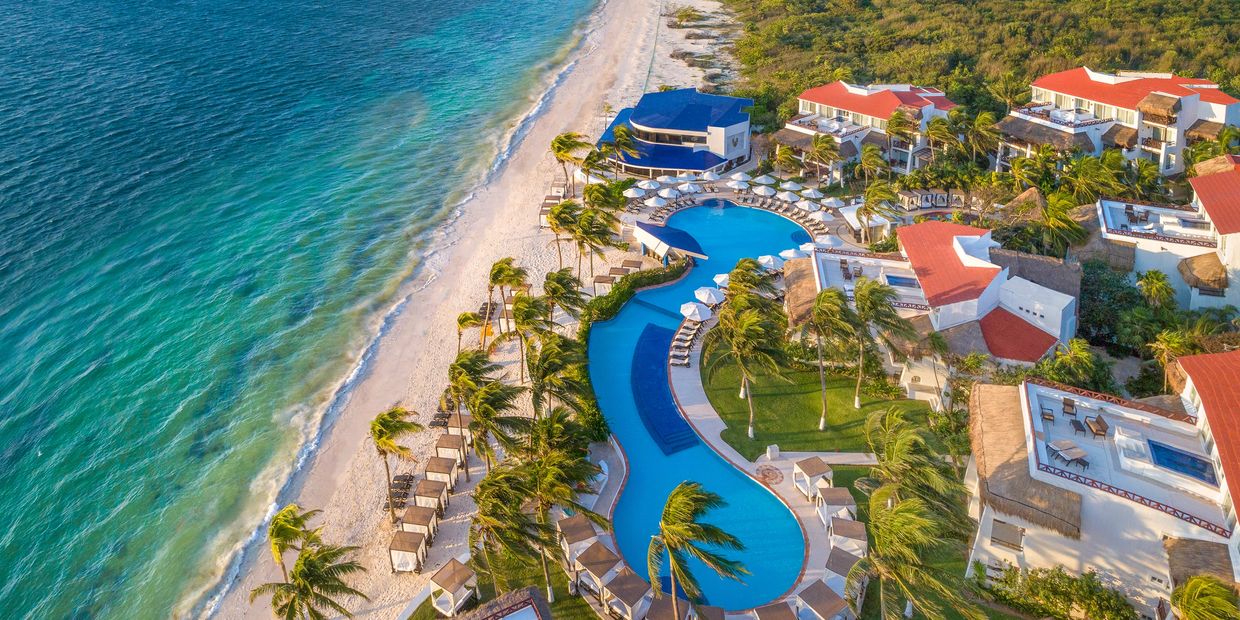 Aerial view of a beachfront resort with pools and palm trees.