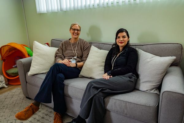 Two mental health clinicians from Healing To You sitting side-by-side on a couch, both smiling.