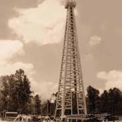Vintage image of a tall wooden oil derrick in a rural setting.