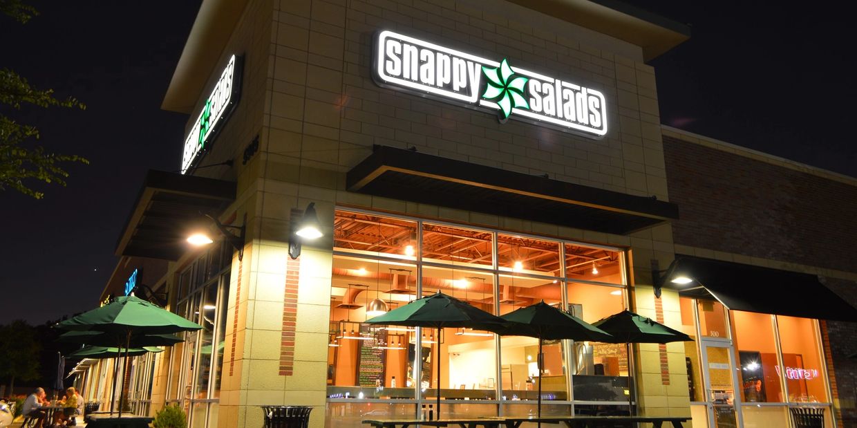 Beautiful exterior of Snappy Salads (Dallas) during the evening with all of the lights on inside