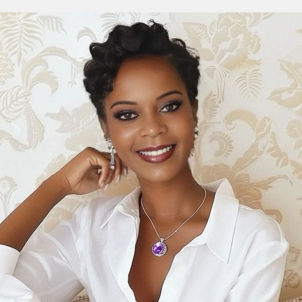 Smiling woman with short curly hair wearing a white blouse and purple pendant necklace.
