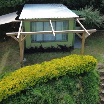 Petite structure en bois avec toiture devant une maison verte.