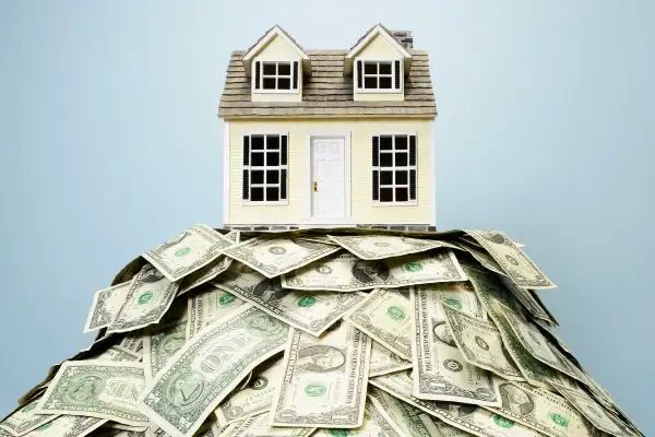 A house model on a pile of dollar bills symbolizing real estate investment.