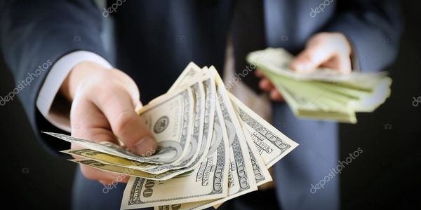 A person in a suit holding and offering US dollar bills.