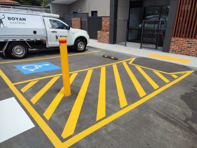 Empty handicapped parking space with bright yellow markings and a white utility truck nearby.
