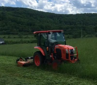 Orange tractor mowing tall grass in a field.