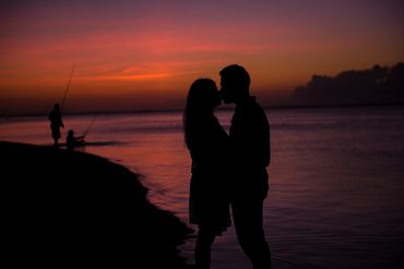 Silhouette photography of couple kissing during sunset with fishermen as backdrop in Mauritius.
