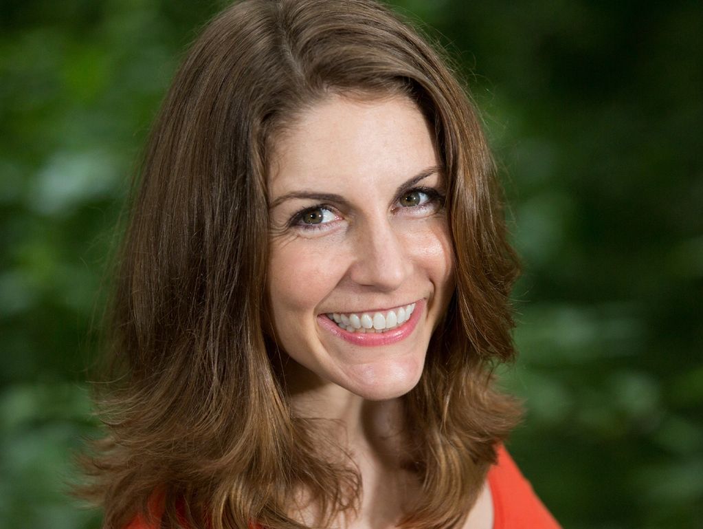 Smiling woman with brown hair in an outdoor setting.