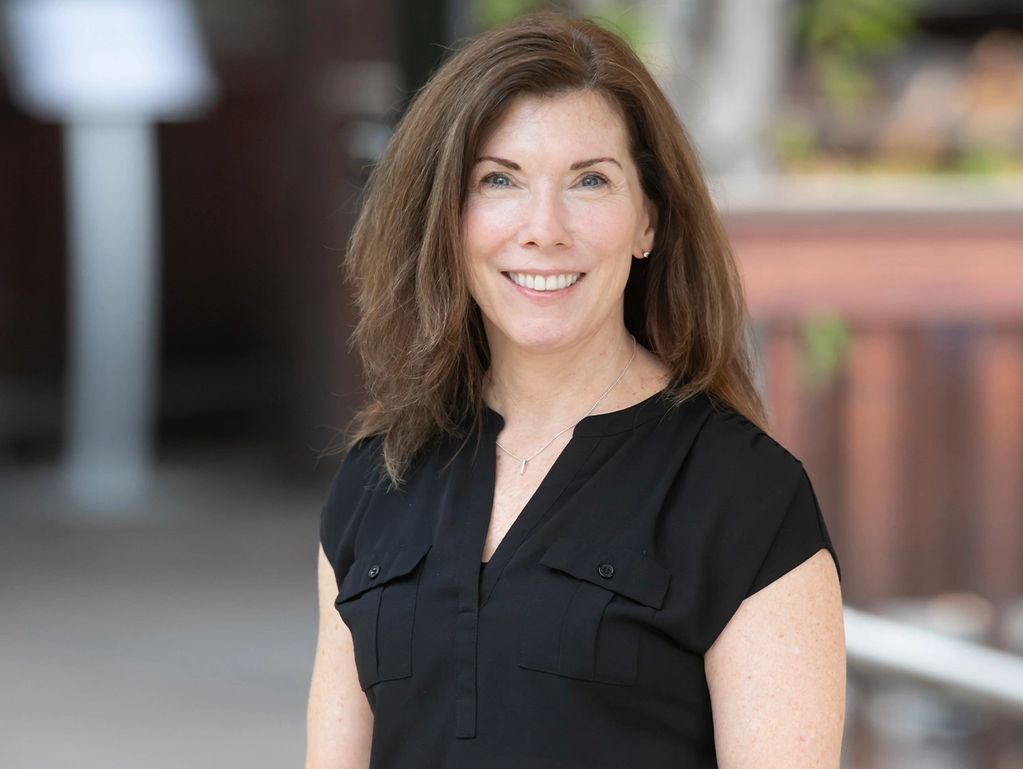 Smiling woman in a black blouse with brown hair outdoors.