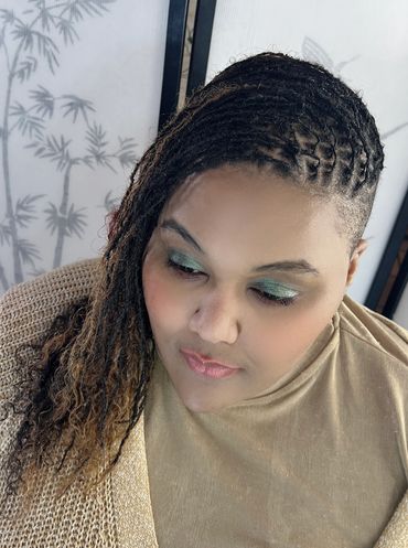 Person with braided hair and green eye shadow looking down.