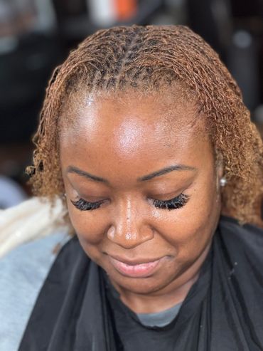 Close-up of a woman with braided hair and long eyelashes looking down.