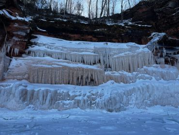 Frozen waterfall with icicles hanging from rocks in a snowy landscape.