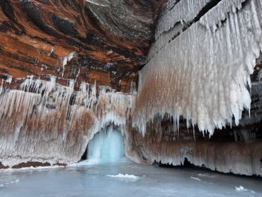 Frozen icicles hanging from a cave ceiling with icy floor below.