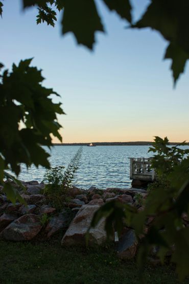 View of a lake through tree leaves at sunset with a dock and distant boat.