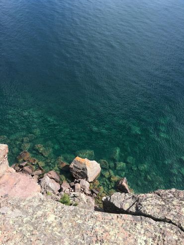 Clear blue water with rocks visible beneath near a rocky shore.