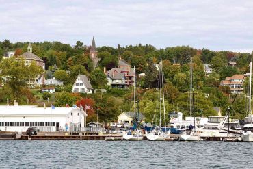 Boats docked at a marina with hillside houses and trees in the background.