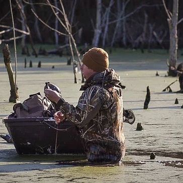 Veteran in camo duck hunting near a duck boat.