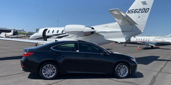 Black sedan parked in front of small plane