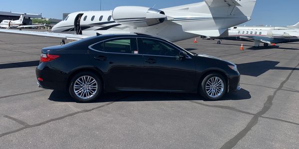 Black sedan parked in front of small plane