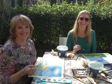 two women sitting at a table painting