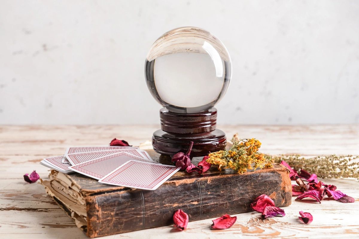 A psychic's crystal ball on top of an old spell book with dried flowers and tarot cards.
