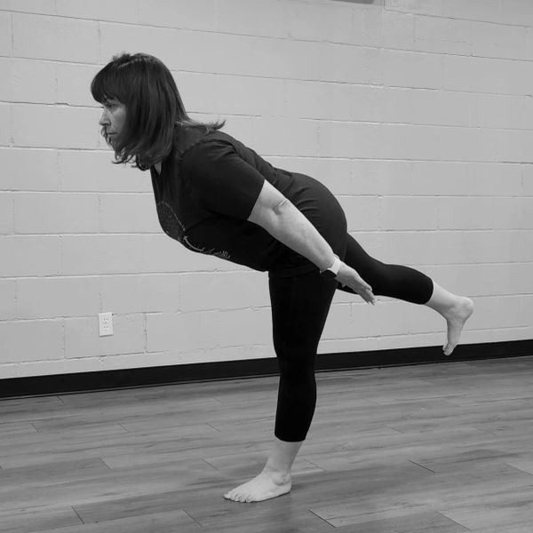 Woman practicing a balancing yoga pose indoors against a brick wall.