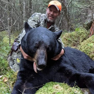 Hunter posing with a large black bear in the forest.