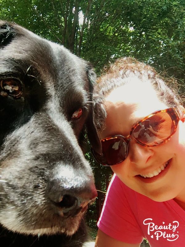 A close-up selfie of a woman and her large black dog outdoors.