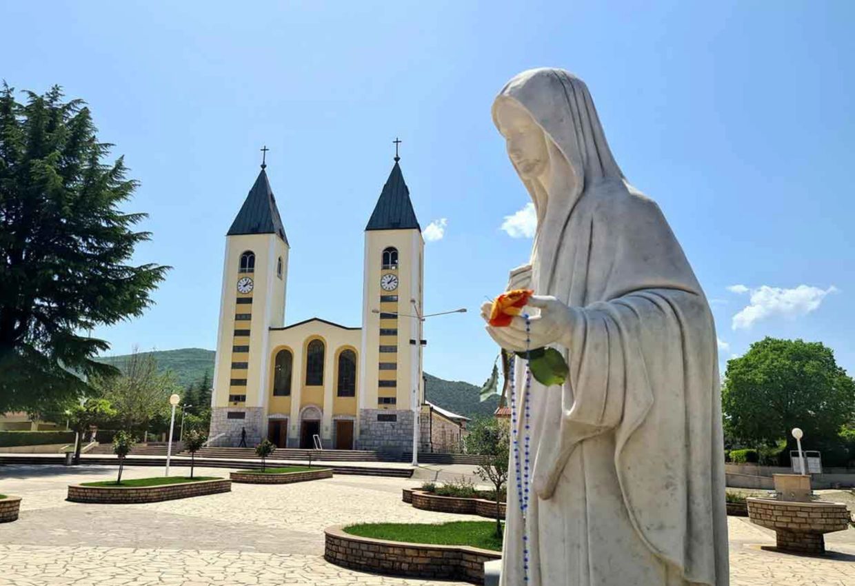 Statue of the Virgin Mary holding a rosary near a church.