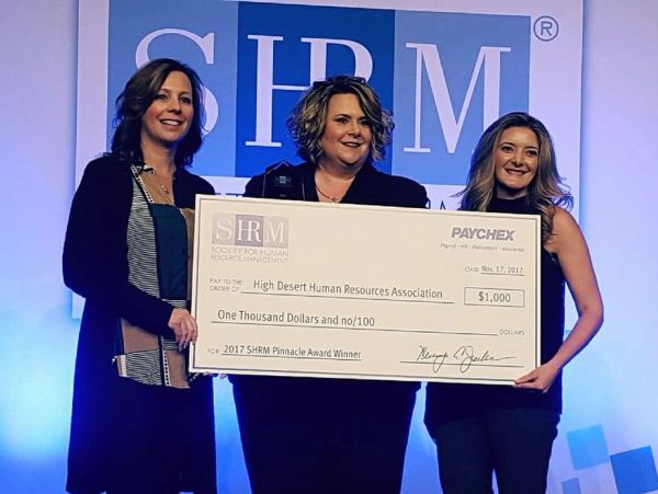 Three women hold a large $1,000 award check at an SHRM event.