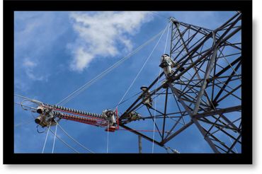 Workers repairing electrical power lines on a tall metal tower against a blue sky.