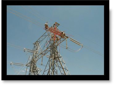 Workers performing maintenance on a high-voltage power transmission tower under clear skies.