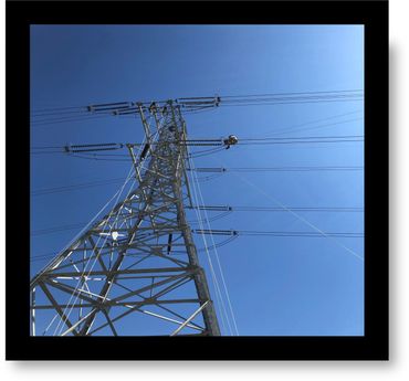 A utility worker repairs power lines atop a transmission tower on a clear day.