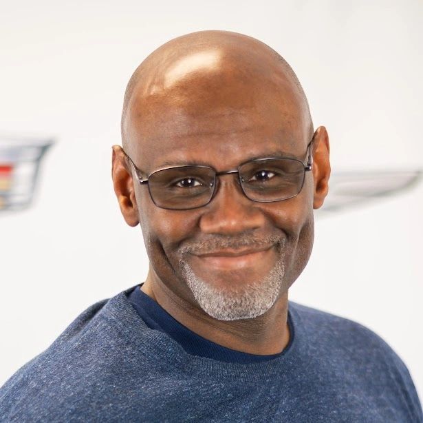 Smiling bald man with glasses in a blue sweater.