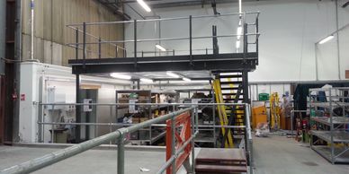 A freestanding storage mezzanine floor with staircase and handrail in an airport workshop.