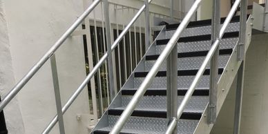 A galvanised steel external fire escape with double tubular handrail and top landing in London.