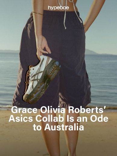 Person holding silver Asics sneaker at the beach with ocean background.