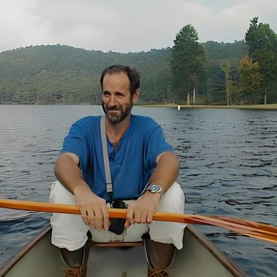 Man rowing a boat on a lake with forested hills in the background.