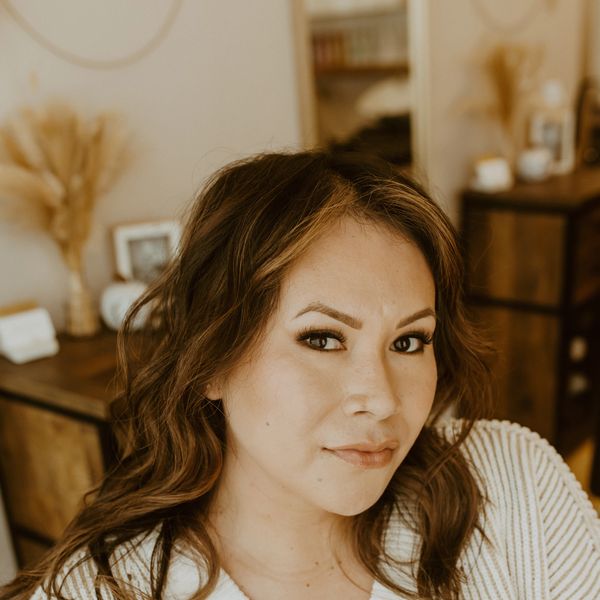 Confident woman with wavy hair poses indoors in warm-toned room.