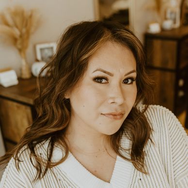 Confident woman with wavy hair poses indoors in warm-toned room.